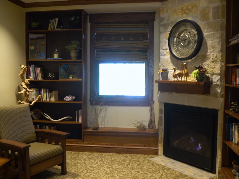 Cozy room with bookshelves, a fireplace, and a clock above the mantel.